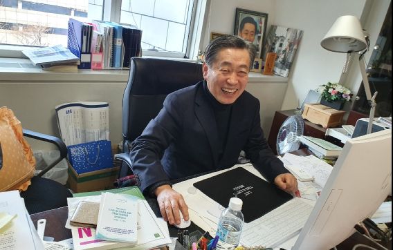 이금룡 이사장이 교대역 근처 사무실 책상에 앉아 활짝 웃고 있다.