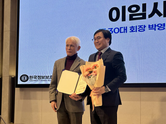 남길현 국방대학교 명예교수(왼쪽)가 한국정보보호학회 학회장 이임식에서 올해 학회장으로 선임된 김호원 부산대 컴퓨터공학과 교수에 이임장 및 꽃다발을 전달하고 있다.