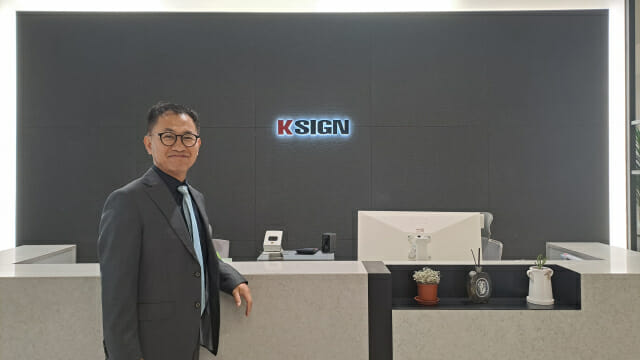 구자동 케이사인 대표가 회사 로고를 배경으로 포즈를 취했다. 올해 케이사인은 PQC와 AI보안에 주력한다.